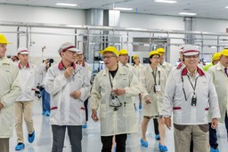 Jensen Huang walking through a Wistron electronics manufacturing plant in a cleanroom smock, accompanied by executives and staff in yellow caps